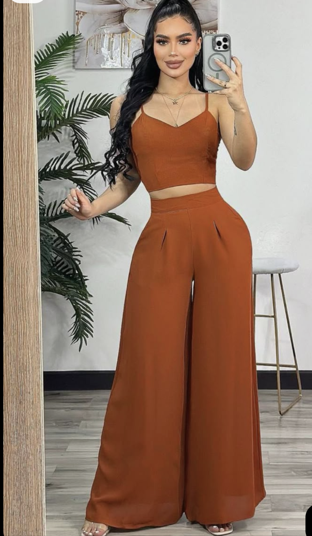 Woman taking a mirror selfie wearing a brown outfit in a room with a plant and stool.